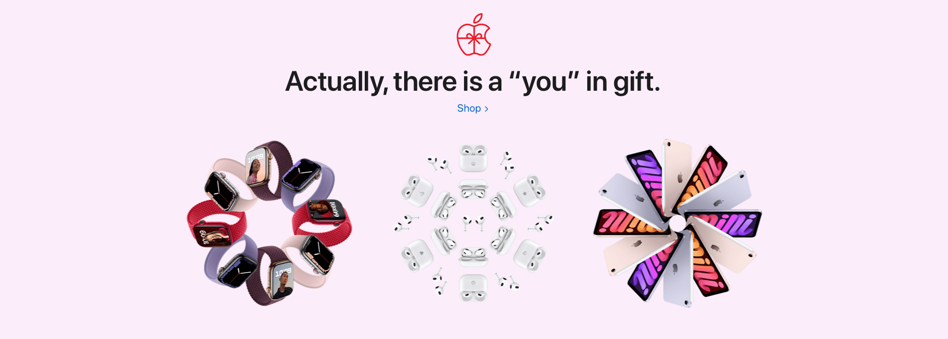 A pink background and the apple logo designed like it's gift wrapped. The phrase says "Actually, there is a "you" in gift. And then beneath are three images of apple products placed in the shape of christmas wreaths. 