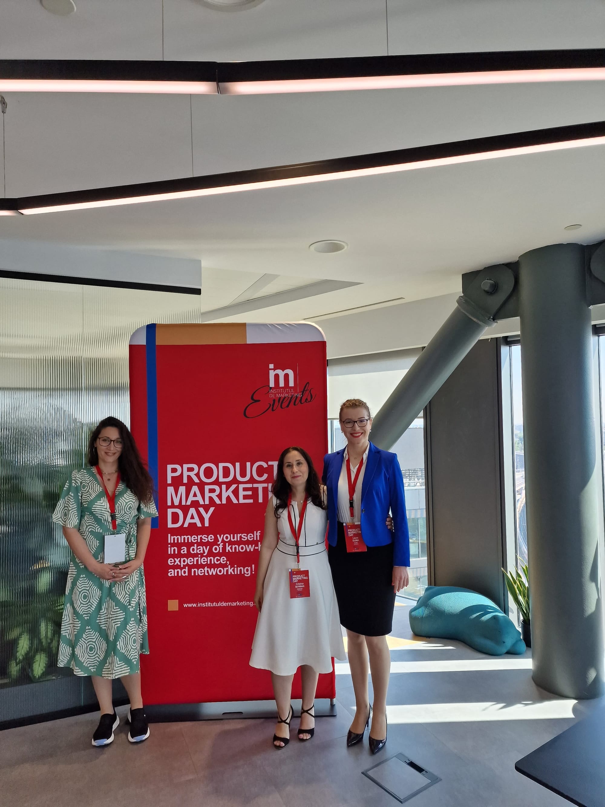 Bianca and two attendees posing in front of the Product Marketing Day banner.